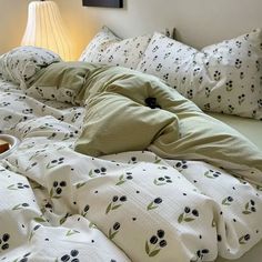 an unmade bed with white sheets and black flowers on it, next to a lamp