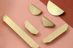 four pieces of gold metal on a pink surface with one piece cut out and the other half closed