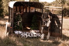 an old horse trailer is decorated with christmas trees and other holiday decorations in the grass