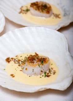 three white plates with scallops covered in sauce and garnishes on them