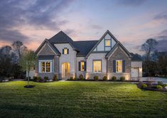 a large house lit up at night with lights on the windows and grass in front