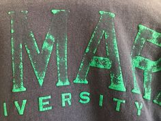 the back of a gray shirt with green letters on it that says imar university