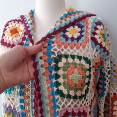 a crocheted granny shawl being held up by a person's hand