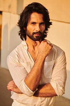 a man with long hair and beard standing in front of a building wearing a white shirt