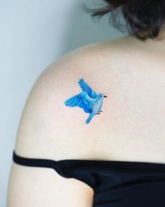 a small blue bird tattoo on the back of a woman's left shoulder and upper arm