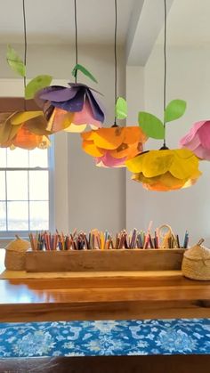 colorful paper flowers hang from the ceiling above a table with pencils and pens on it