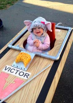 a baby in a mouse costume sitting on top of a wooden table with cheese and crackers