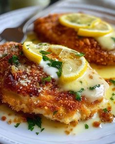 two pieces of chicken with lemon and parmesan cheese on a white dinner plate