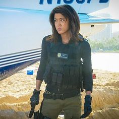 a woman standing in front of an airplane on the beach with her hands in her pockets