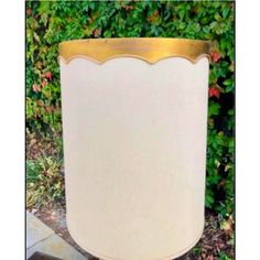 a large white and gold vase sitting on top of a wooden table next to bushes