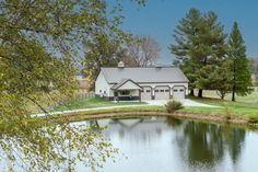 a house with a pond in front of it and trees around the lake side area