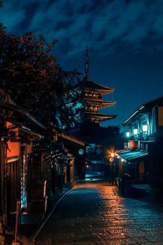 an empty street at night with lanterns lit up on the buildings and trees in the background