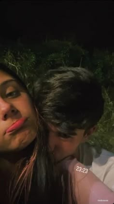 two people that are kissing each other in front of some trees and bushes at night