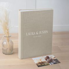 a wedding album next to a vase filled with dried flowers and a couple's photo