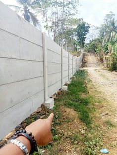 a hand pointing towards a concrete wall with grass and trees in the backround