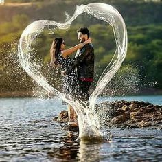 a man and woman are standing in the water with their arms around each other as they make a heart shape