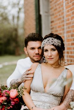 a tattooed bride and groom sitting on a bench in front of a brick building with flowers