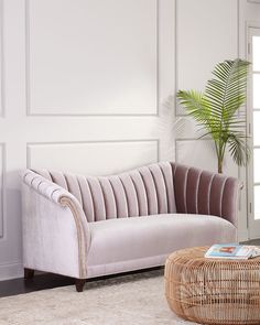 a living room with a wicker coffee table and pink velvet couch in front of a white paneled wall