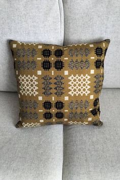 a brown and black pillow sitting on top of a gray couch next to a white wall