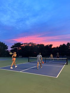 people are playing tennis on a court at sunset or dawn with trees in the background