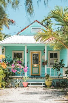 a blue house with white trim and flowers on the front porch is surrounded by palm trees