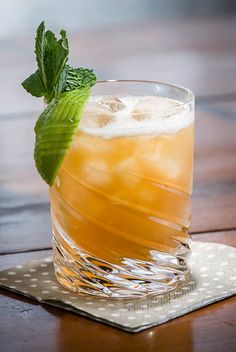 a close up of a drink in a glass on a table with a green garnish