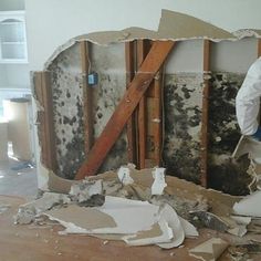 a man in a white shirt is working on a wall with moldy paint and wood