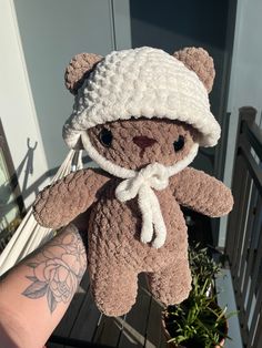 a teddy bear wearing a white hat and scarf is held in someone's hand