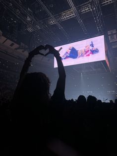 a person holding up a heart shaped hand in front of a crowd at a concert