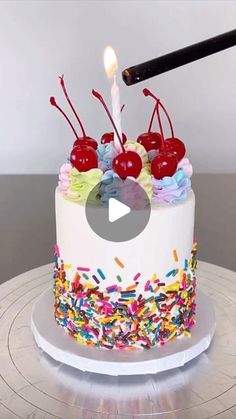 a white cake with sprinkles and cherries on it, topped with a lit candle