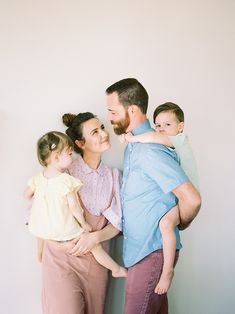 a man, woman and two children standing in front of a white wall with their arms around each other