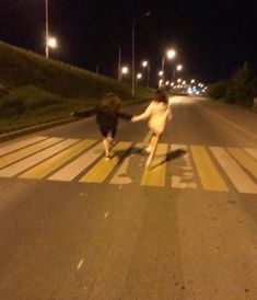 two people crossing the street at night with their hands in each other's pockets