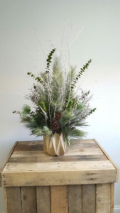 a wooden table topped with a vase filled with greenery and pine cone shaped planters