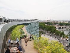 people are sitting at tables on the side of a building overlooking a river and bridge