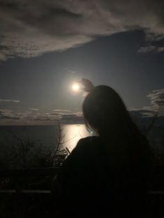 a woman is looking at the moon over the ocean with her hand up in the air