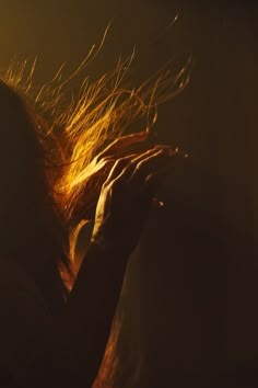 a woman with her hair blowing in the wind on a dark background and light coming from behind