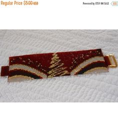 a red and gold bracelet with a christmas tree design on it's side, sitting on a white surface