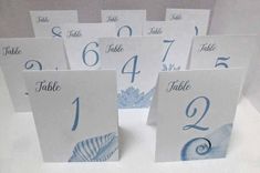 table numbers and place cards are displayed on a white surface with blue seashells