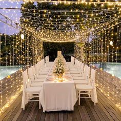 a long table is set up with white chairs and lights strung over the place setting