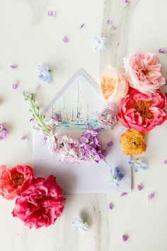 some flowers are laying on top of an envelope with a sailboat in the background