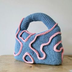 a crocheted blue purse sitting on top of a wooden table next to a white wall