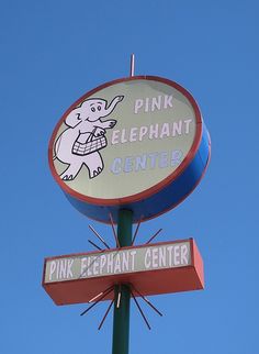 a pink elephant center sign on top of a green pole with two signs below it