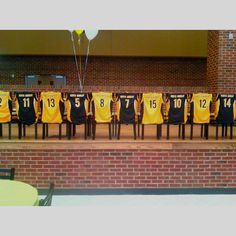 a row of chairs with yellow and black jerseys on them in front of a brick wall