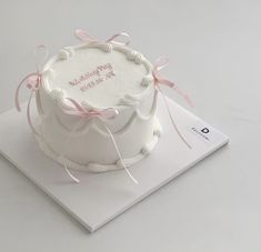 a white cake with pink ribbon on top