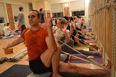 a group of people sitting on yoga mats in a room with ropes hanging from the ceiling