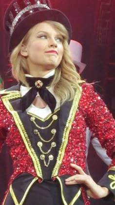 a woman wearing a red and black outfit with a crown on her head, standing in front of a stage