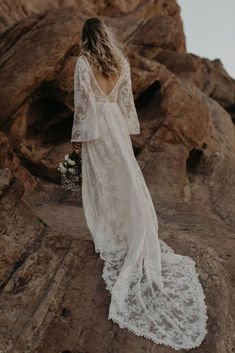 a woman standing on top of a rocky hill wearing a white dress and holding a bouquet