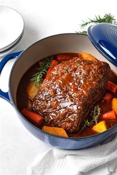 a pot filled with meat and carrots on top of a white cloth next to two plates