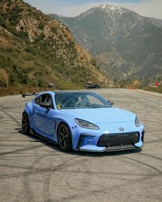 a blue sports car parked on the side of a road in front of some mountains