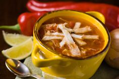 a yellow bowl filled with soup next to red peppers and limes on a wooden table